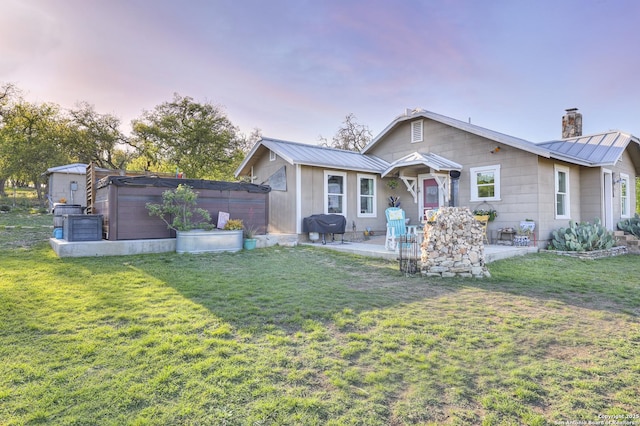283 N Second St, Harper, TX 78631 - back of property at dusk with a lawn, a chimney, a patio, and metal roof
