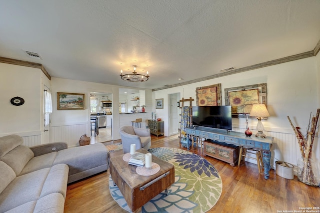 283 N Second St, Harper, TX 78631 - living area featuring wood finished floors, a textured ceiling, an inviting chandelier, a wainscoted wall, and visible vents