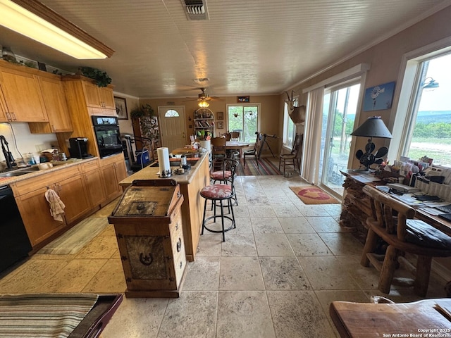 kitchen featuring an island with sink, stone tile floors, a ceiling fan, visible vents, and black appliances