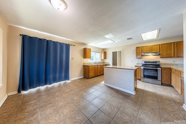 kitchen with stainless steel range with electric stovetop, under cabinet range hood, brown cabinetry, a center island, and light countertops