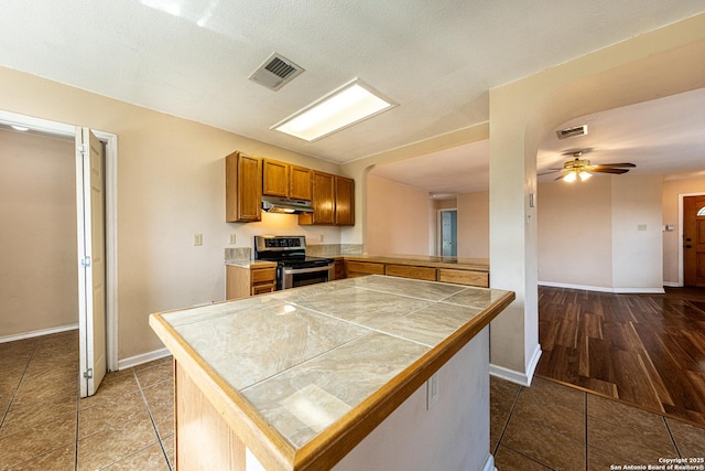 kitchen with a ceiling fan, stainless steel electric stove, under cabinet range hood, and visible vents