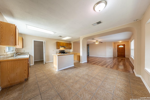 kitchen with under cabinet range hood, a center island, visible vents, arched walkways, and open floor plan