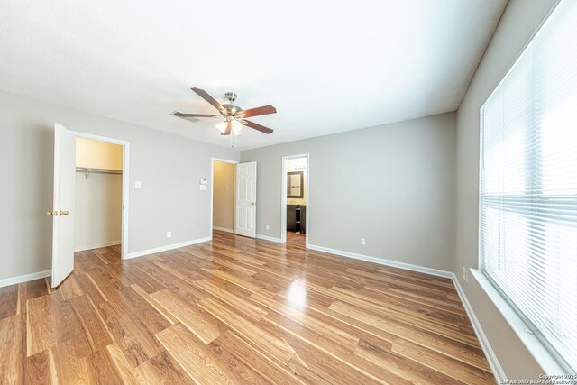 unfurnished bedroom featuring a walk in closet, light wood-style floors, baseboards, and multiple windows