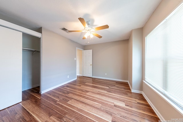 unfurnished bedroom featuring wood finished floors, multiple windows, visible vents, and a closet