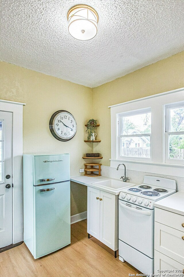 kitchen featuring light countertops, a sink, white appliances, light wood-style floors, and a textured ceiling