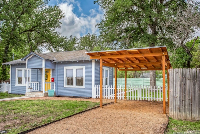 view of front of home with a front lawn, roof with shingles, fence, and a carport