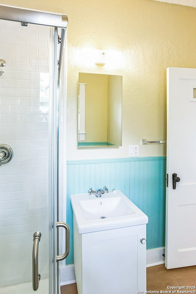 bathroom with a shower stall, a wainscoted wall, and vanity
