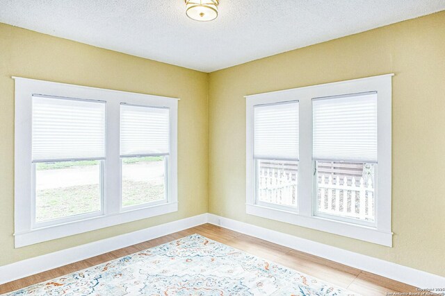 empty room with light wood finished floors, baseboards, and a textured ceiling
