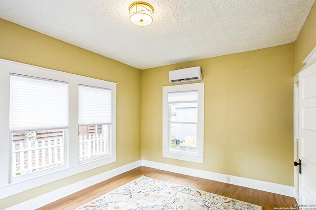 unfurnished room featuring baseboards, wood finished floors, a wall mounted AC, and a textured ceiling