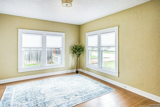 spare room featuring baseboards, a textured wall, wood finished floors, and a textured ceiling