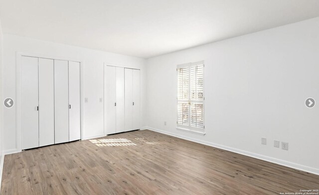 unfurnished bedroom with two closets, baseboards, and wood finished floors