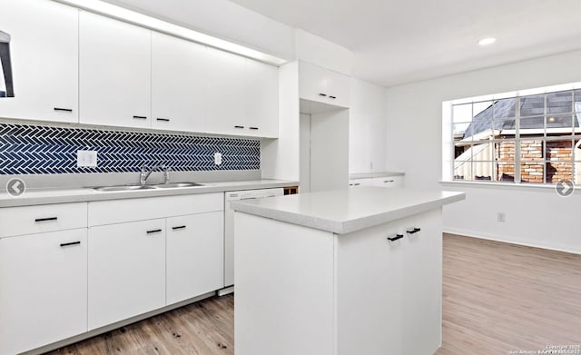 kitchen with a center island, a sink, decorative backsplash, light wood finished floors, and light countertops