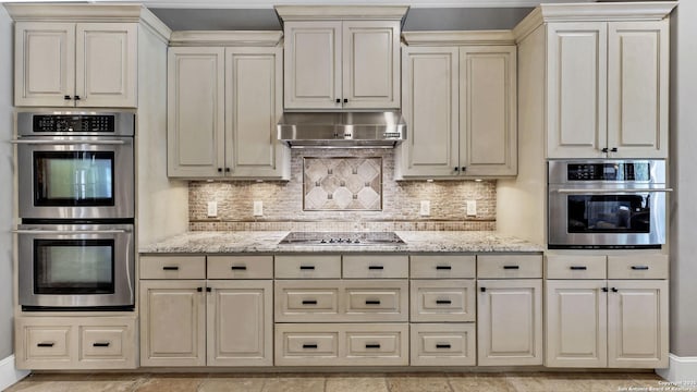 kitchen with double oven, light stone countertops, cream cabinetry, and black electric stovetop