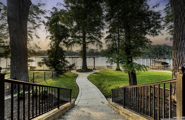 view of community with a yard, a water view, and fence