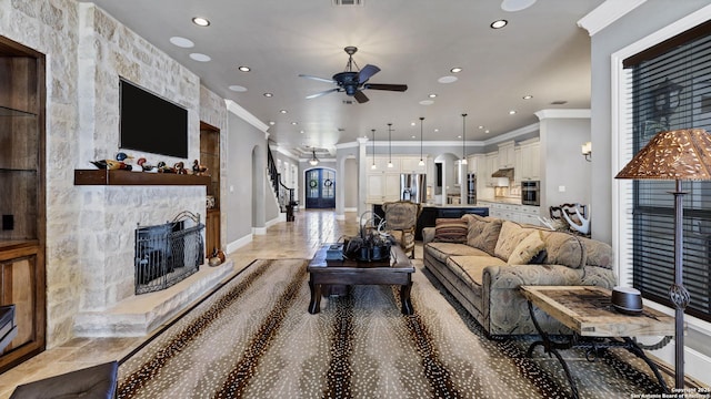 living room with a stone fireplace, ceiling fan, arched walkways, ornamental molding, and recessed lighting