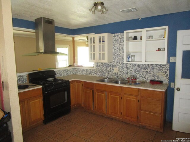 kitchen featuring gas stove, island exhaust hood, a sink, and tasteful backsplash