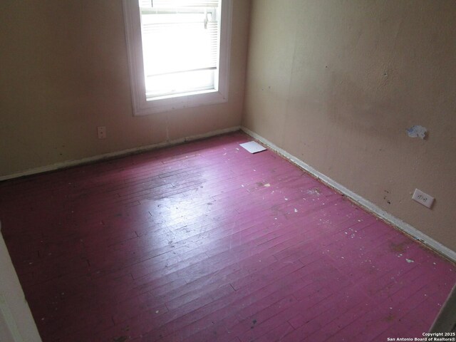 spare room featuring wood-type flooring and baseboards