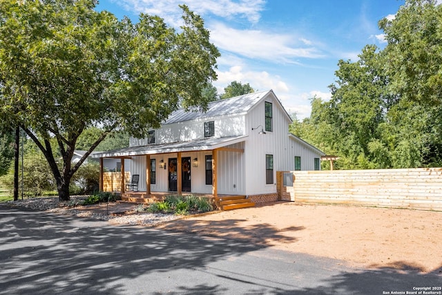 modern farmhouse style home with board and batten siding, fence, metal roof, and covered porch