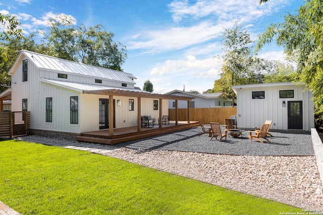 rear view of house featuring fence, a yard, board and batten siding, a wooden deck, and an outdoor fire pit