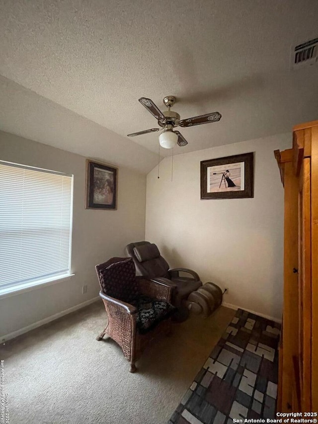living area featuring visible vents, a ceiling fan, carpet floors, baseboards, and a textured ceiling