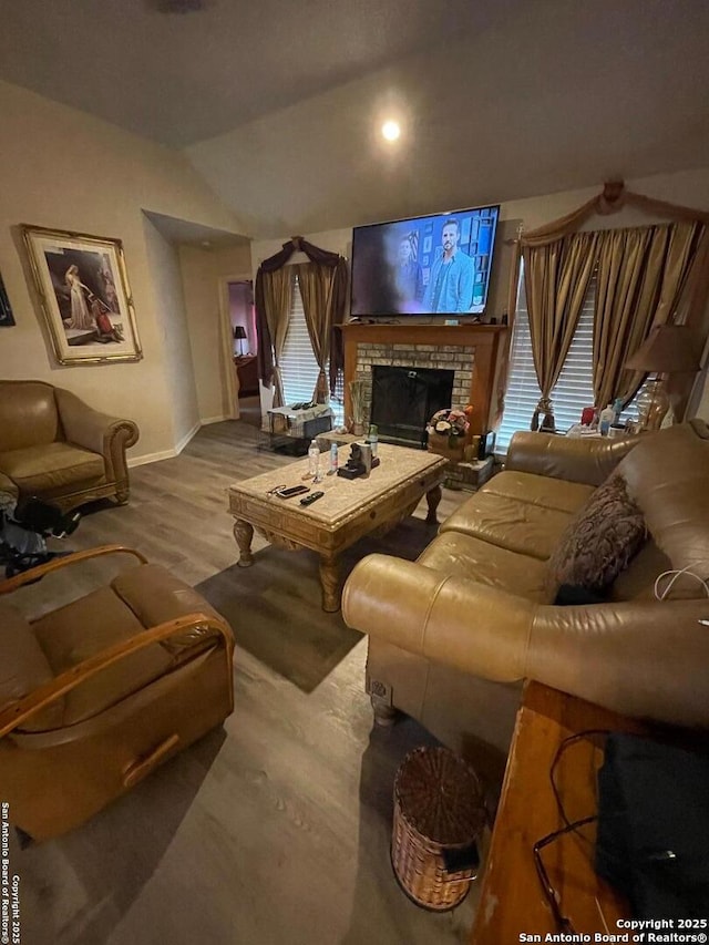 living room featuring lofted ceiling, wood finished floors, baseboards, and a brick fireplace