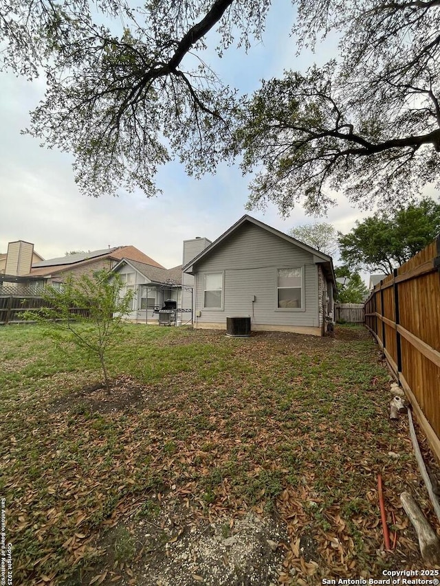 back of house with a lawn, a fenced backyard, and central AC unit