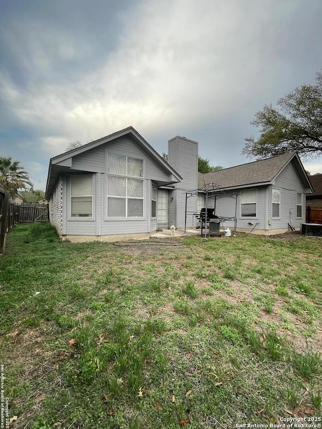 back of property featuring a chimney, fence, and a lawn