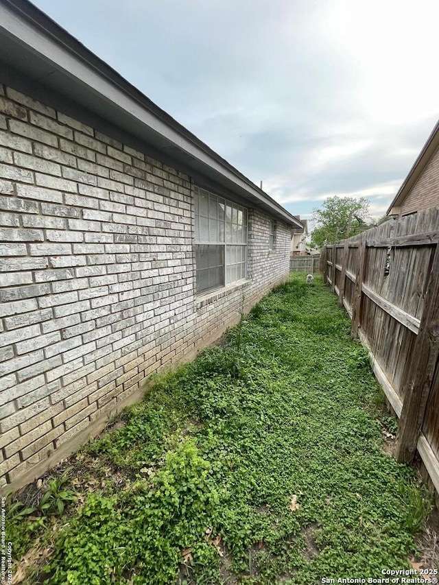 view of side of property featuring brick siding, a lawn, and fence