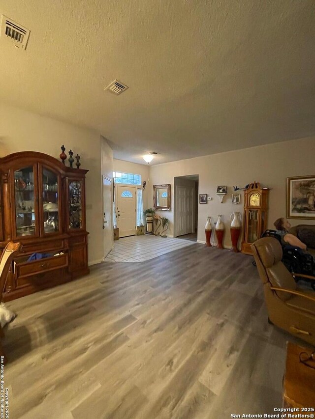 interior space with wood finished floors, a textured ceiling, baseboards, and visible vents