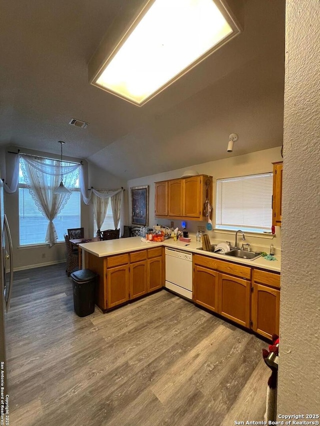 kitchen with light countertops, dishwasher, a sink, a peninsula, and light wood-style flooring