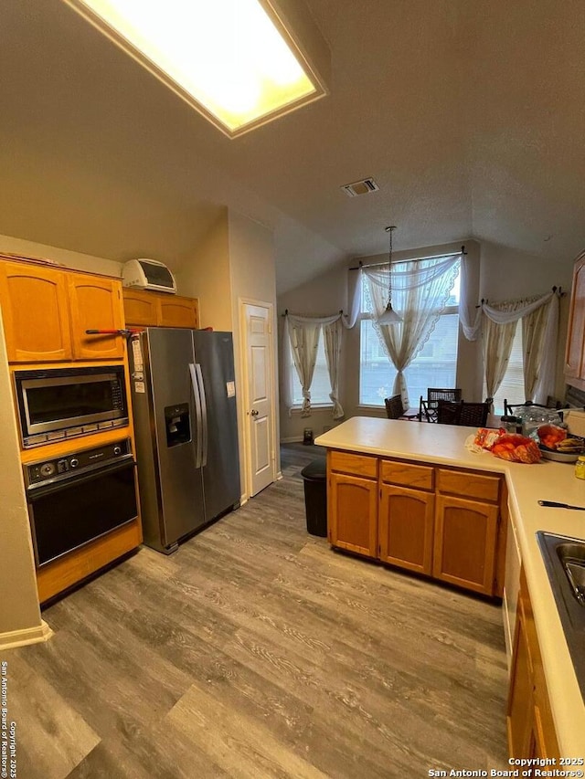 kitchen featuring built in microwave, visible vents, lofted ceiling, stainless steel refrigerator with ice dispenser, and black oven