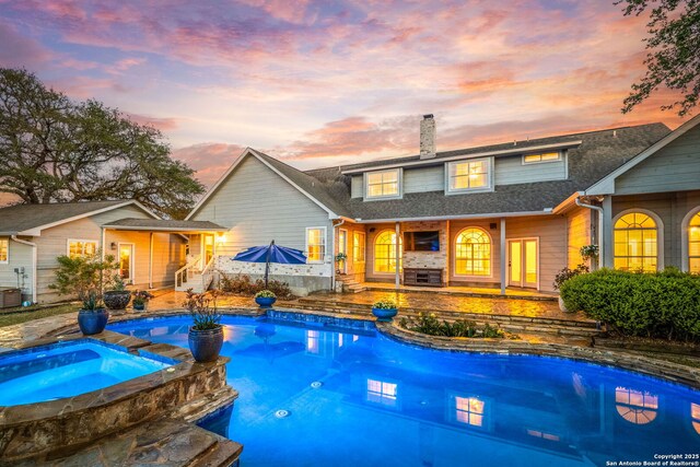 pool at dusk with a patio area and a pool with connected hot tub