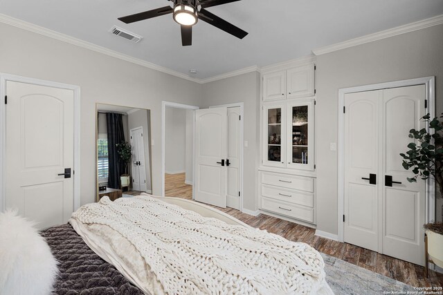 bedroom featuring baseboards, visible vents, light wood-style floors, two closets, and crown molding