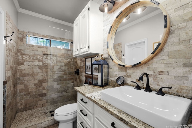 bathroom with a tile shower, vanity, ornamental molding, and toilet