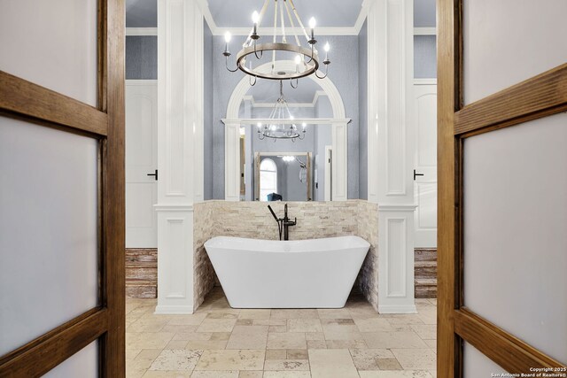 bathroom with stone tile flooring, a soaking tub, ornamental molding, and an inviting chandelier