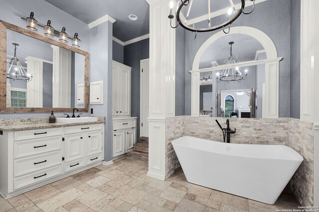 full bath featuring stone tile floors, an inviting chandelier, a freestanding bath, vanity, and wainscoting