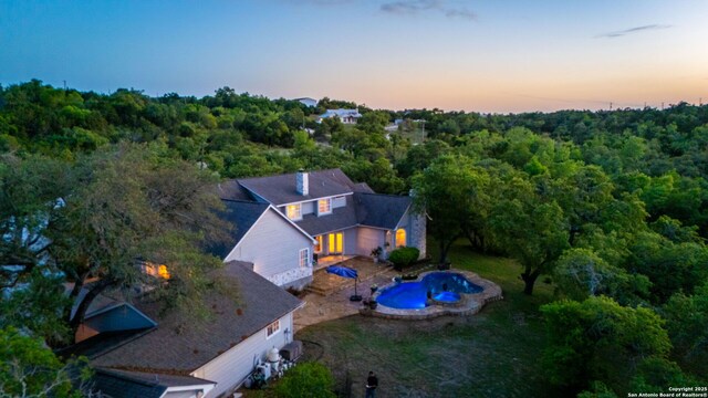aerial view at dusk featuring a wooded view