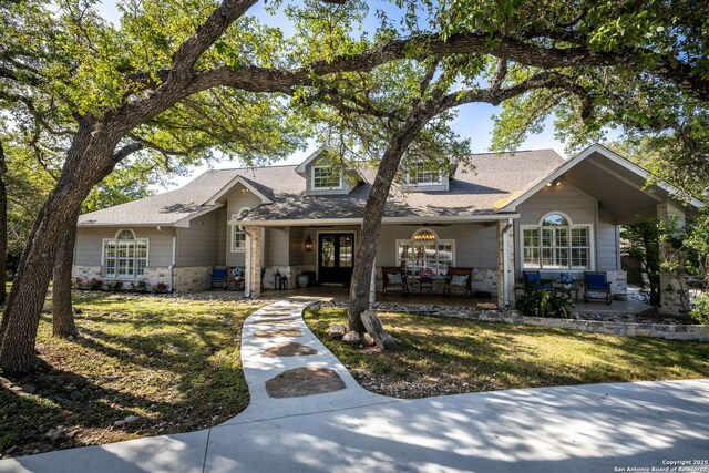 view of front facade with stone siding, a shingled roof, a front lawn, and covered porch
