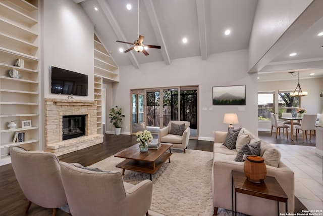 living room with high vaulted ceiling, a stone fireplace, ceiling fan with notable chandelier, built in shelves, and beamed ceiling