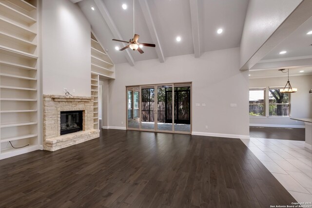 unfurnished living room with ceiling fan with notable chandelier, baseboards, wood finished floors, and a fireplace