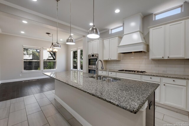 kitchen with white cabinets, a sink, backsplash, custom range hood, and appliances with stainless steel finishes