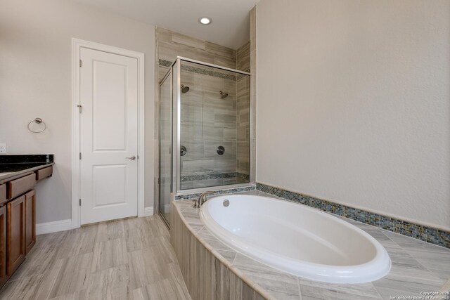 bathroom with a stall shower, baseboards, recessed lighting, a garden tub, and vanity