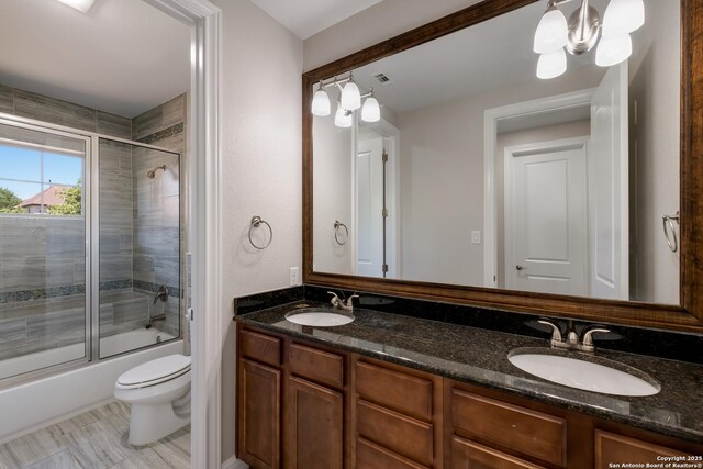 full bathroom featuring shower / bath combination with glass door, double vanity, toilet, and a sink
