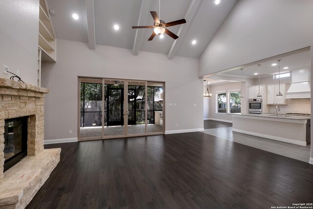 unfurnished living room with a ceiling fan, dark wood-type flooring, beam ceiling, a fireplace, and high vaulted ceiling