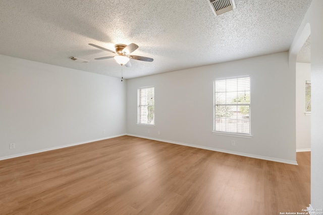 spare room featuring light wood finished floors, visible vents, a textured ceiling, and ceiling fan