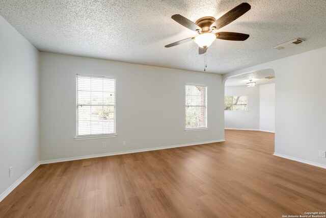 unfurnished room with arched walkways, a textured ceiling, a healthy amount of sunlight, visible vents, and ceiling fan