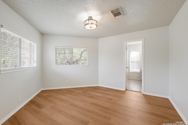 spare room featuring a textured ceiling, light wood-type flooring, a healthy amount of sunlight, and visible vents