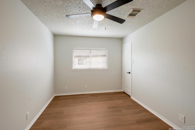empty room with a textured ceiling, baseboards, visible vents, wood finished floors, and ceiling fan