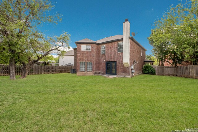 rear view of property with a chimney, brick siding, a yard, and french doors