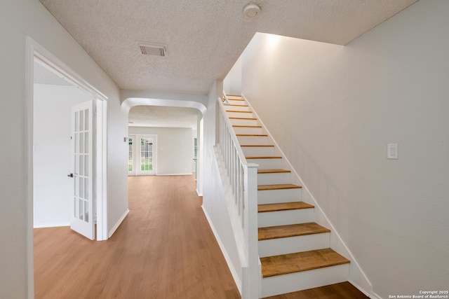 stairway with wood finished floors, visible vents, arched walkways, and a textured ceiling